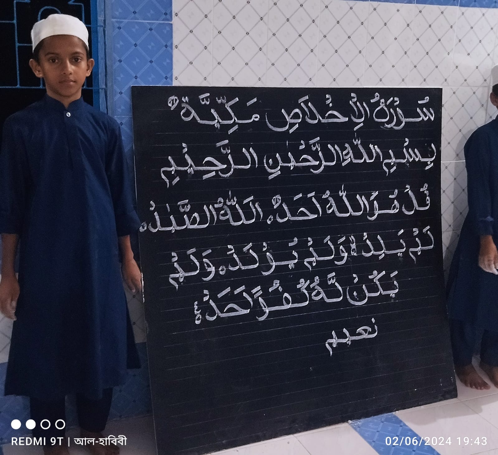 Student displaying Surah Al-Ikhlas written on a blackboard
